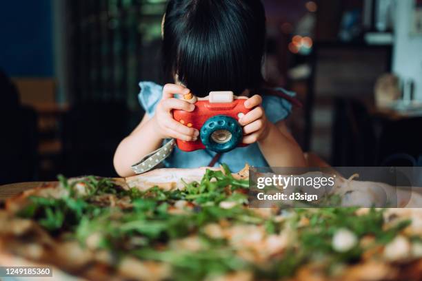 cute little asian girl playing with her wooden toy camera and taking a picture of a giant pizza in a restaurant - day in the life stock pictures, royalty-free photos & images