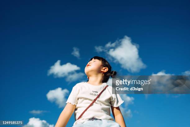 cute little asian girl with eyes closed enjoying the warmth of sun and the gentle breeze against beautiful blue sky on a lovely sunny day - kid looking up stock pictures, royalty-free photos & images