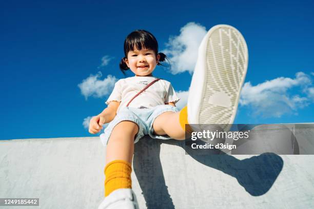 low angle view of cute little asian girl smiling joyfully and having fun in outdoor park against beautiful blue sky on a lovely sunny day - only kids at sky stockfoto's en -beelden