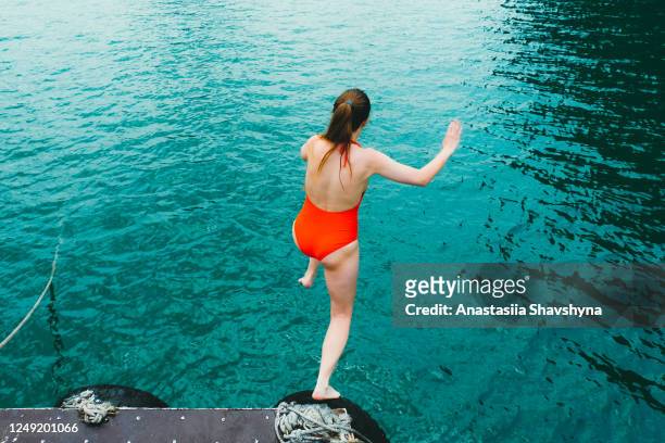 young woman in red swimsuit jumping into the bright turquoise sea - meet the summertime! - jumping into water stock pictures, royalty-free photos & images