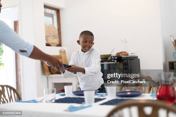 mother hands plates to son as he sets the dinner table - setting the table stock pictures, royalty-free photos & images