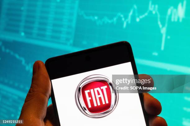 In this photo illustration, the Italian automobile manufacturer Fiat logo seen displayed on a smartphone with an economic stock exchange index graph...