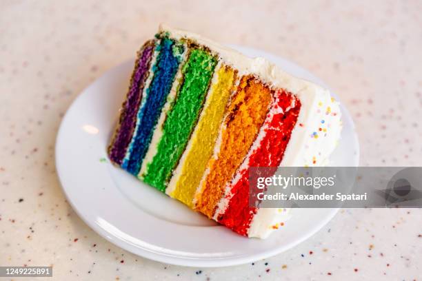 slice of rainbow cake on a plate - taartpunt stockfoto's en -beelden