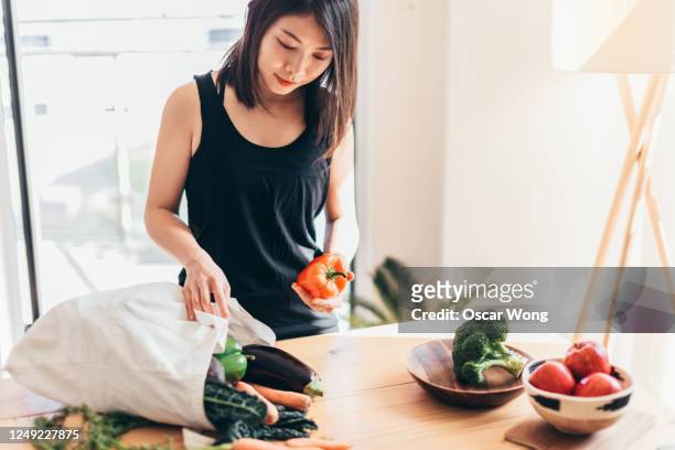 young woman organising groceries after shopping - crucifers stock pictures, royalty-free photos & images