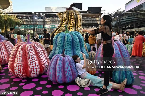 People take pictures of sculptures by Japanese artist Yayoi Kusama in collaboration with Louis Vuitton outside of a shopping mall in Bangkok on March...