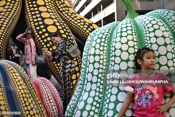 People take pictures of sculptures by Japanese artist Yayoi Kusama in collaboration with Louis Vuitton outside of a shopping mall in Bangkok on March...