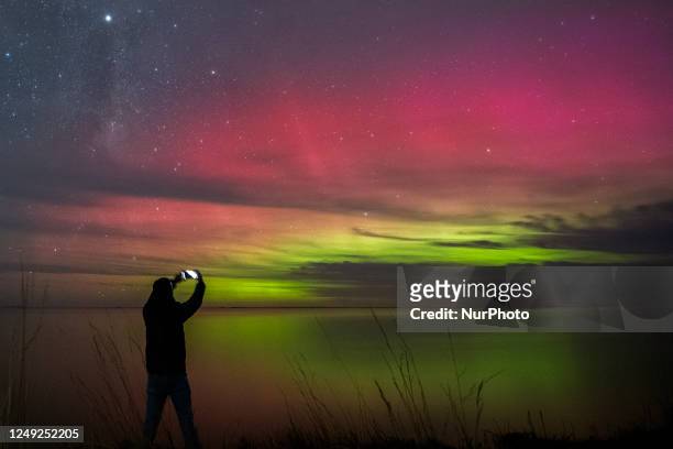 Man takes pictures of the Aurora, also known as the southern lights, glow on the horizon over the waters of Selwyn Lake in Selwyn Huts, in the...