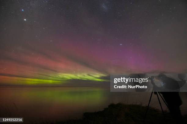 Photographer takes pictures of the Aurora, also known as the southern lights, glow on the horizon over the waters of Selwyn Lake in Selwyn Huts, in...