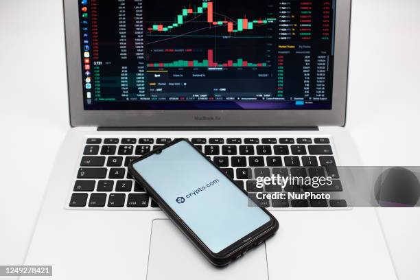 In this photo illustration a Crypto.com logo seen displayed on a smartphone screen and an Exchange graph on a MacBook screen in Athens, Greece on...