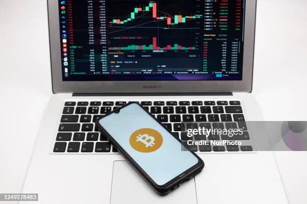 In this photo illustration a Bitcoin logo seen displayed on a smartphone screen and an Exchange graph on a MacBook screen in Athens, Greece on March...