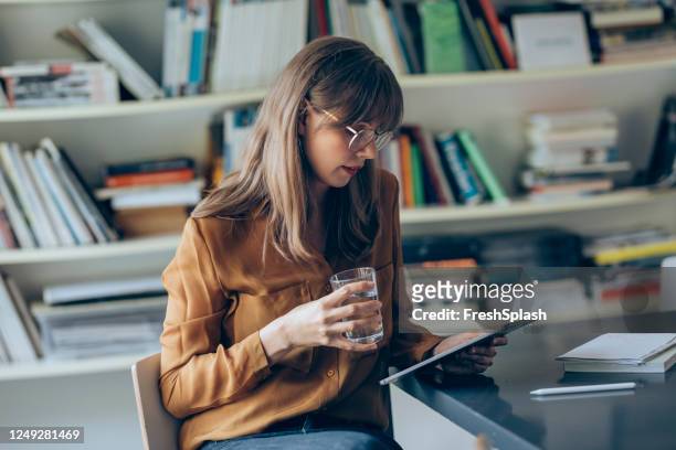 geschäftsfrau trägt brille und ein gelbes hemd lesen etwas auf einem digitalen tablet im büro - library　woman stock-fotos und bilder