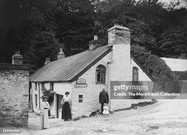 Two well dressed women standing with the postmaster with a dog and young child by his side in front of Simonsbath post office;Simonsbath, Exmoor in...