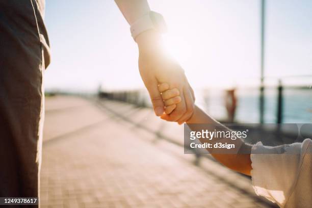 close up of young asian mother walking hand in hand with her little daughter enjoying family bonding time in a park along the promenade at sunset - kindertijd stockfoto's en -beelden