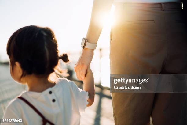 cropped shot of young asian mother walking hand in hand with her cute little daughter, enjoying family bonding time in a park along the promenade at sunset - asia ray stock-fotos und bilder