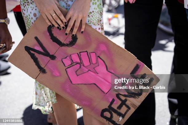 Caucasian protester holds in their hands homemade sign on a box that says, "No Peace" with a pink version of the black power fist during a protest at...