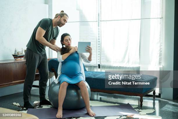 pregnancy home workout for good health. husband with beard help his pregnant wife practicing exercise on gym ball while watching online prenatal care at home. - prenatal care stock pictures, royalty-free photos & images