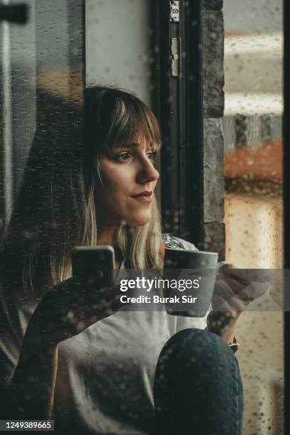raindrops, woman looking out the window and drinking coffee - rainy day window stock pictures, royalty-free photos & images