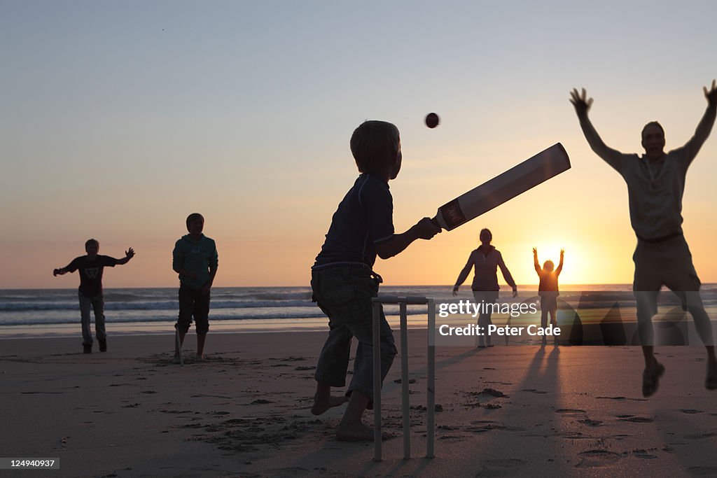 Family playing cricket on beach at sunset