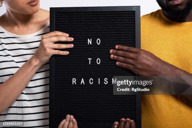 onherkenbaar afro-amerikaans echtpaar poseren in een studio met een teken "nee tegen racisme" - antiracisme stockfoto's en -beelden