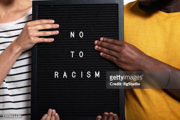 onherkenbaar afro-amerikaans echtpaar poseren in een studio met een teken "nee tegen racisme" - antiracisme stockfoto's en -beelden
