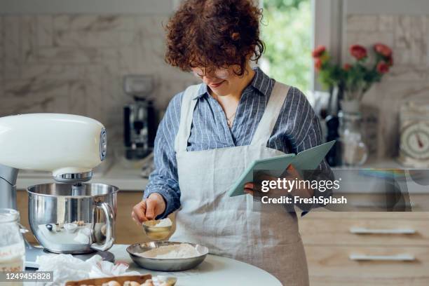 baking cookies: een lachende vrouw na een live cooking video sessie online tijdens het maken van cookies thuis - baking reading recipe stockfoto's en -beelden