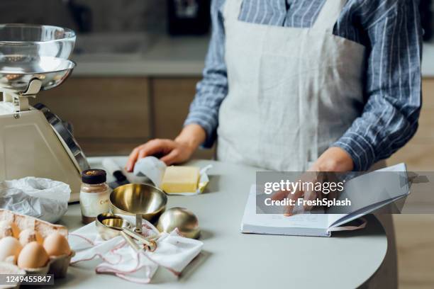 bakken thuis: een jonge vrouw het lezen van een recept uit haar receptenboek in de keuken - baking reading recipe stockfoto's en -beelden