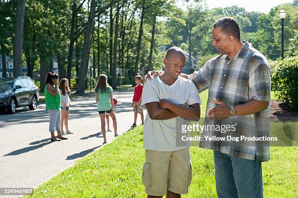 father consoling son with kids playing behind - kickball stock pictures, royalty-free photos & images