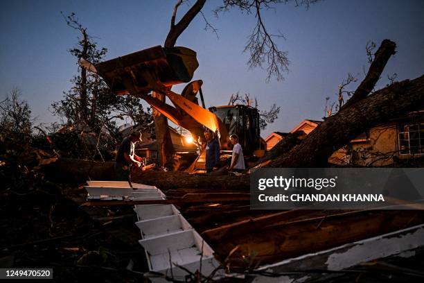 People cut down a fallen tree in the backyard of their house in Rolling Fork, Mississippi, on March 25 after a tornado touched down in the area. - At...