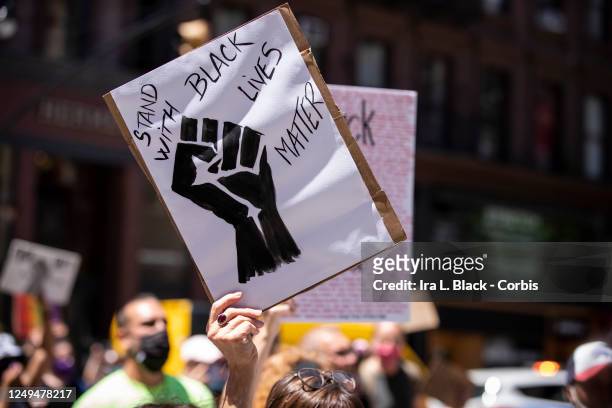 Caucasian protester holds a homemade sign that says, "Stand With Black Lives" with a black power fist during a protest with hundreds of people that...