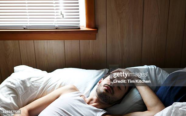 cute latin guy sleeping in bed near window - hangover stockfoto's en -beelden