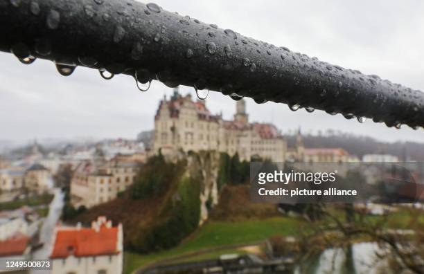 March 2023, Baden-Württemberg, Sigmaringen: Raindrops hang from a railing of a viewing platform, while Sigmaringen Castle, also called Hohenzollern...