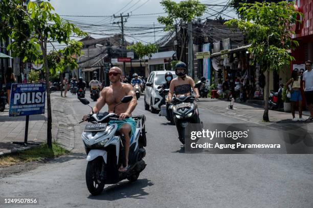 Foreigner tourist rides a motorcycle without helmet and shirt at a main road on March 26, 2023 in Canggu, Bali, Indonesia. Indonesian island of the...