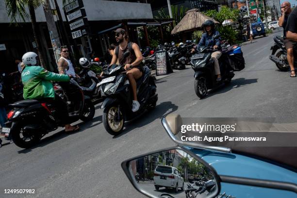 Foreigner tourist rides a motorcycle without helmet at a main road on March 26, 2023 in Canggu, Bali, Indonesia. Indonesian island of the gods plans...