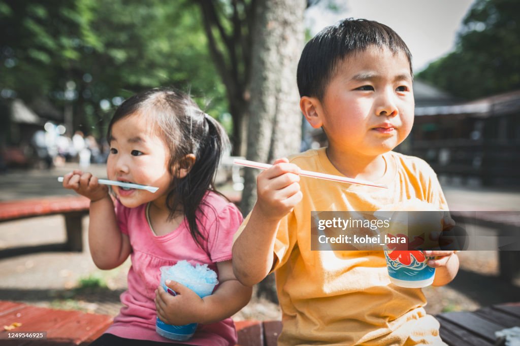 Siblings eating shaved ice in the park