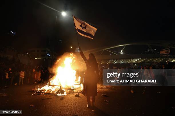 Protesters block a road and hold national flags as they gather around a bonfire during a rally against the Israeli government's judicial reform in...