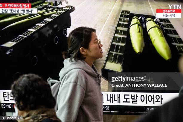 Woman walks past a television showing a news broadcast with file footage of missiles during a North Korean military parade, at a railway station in...