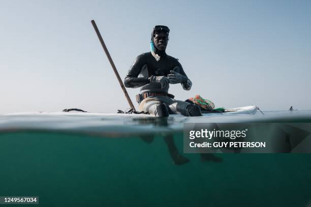 Brahem sits on his paddle board used to hold equipment after a dive hunting for fish and crustaceans in the shallow water off the coast of Dakar on...