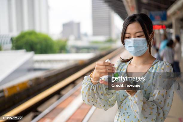 an asian chinese with face mask sanitzing hands with hand sanitizer at train station - hand sanitiser stock pictures, royalty-free photos & images