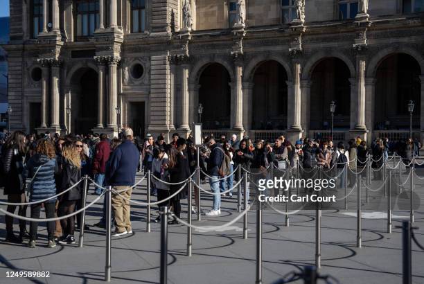 Tourists queue to enter the Louvre Museum as striking union members form a picket line outside the museum entrance on March 27, 2023 in Paris,...