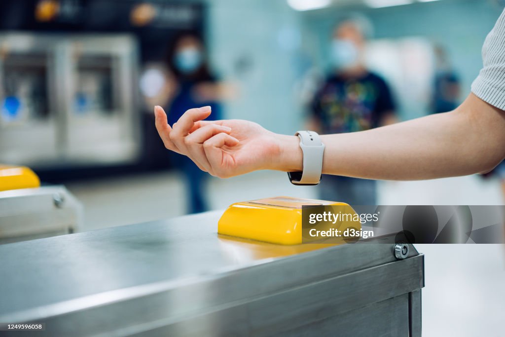 Cropped shot of young Asian woman checking in at subway station using contactless payment for subway ticket via smartwatch