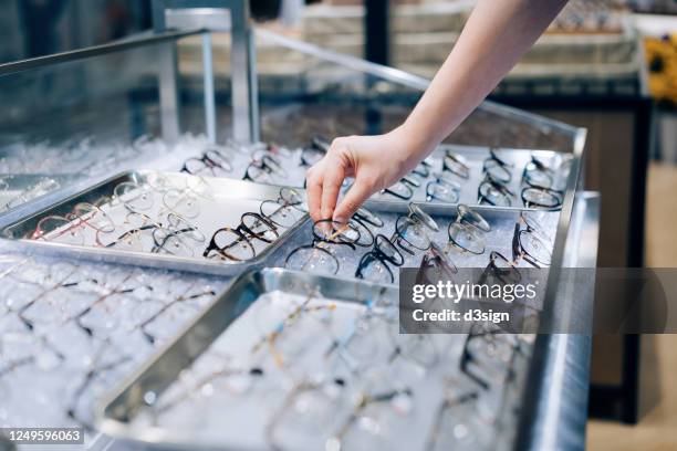 cropped shot of young asian woman selecting eye glasses from retail display in optical shop - lens optical instrument stock pictures, royalty-free photos & images