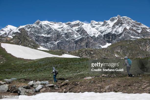 Two people without protective masks trek on a mountain path with the background of the mountains inside the Gran Paradiso national park on June 14,...