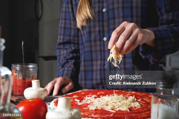 cooking italian vegetarian pizza with vegetables and mushrooms at home, on a wooden table. the woman puts and sprinkles grated cheese on the dough. step-by-step instructions, do it yourself. step 4. - molho de sobremesa imagens e fotografias de stock