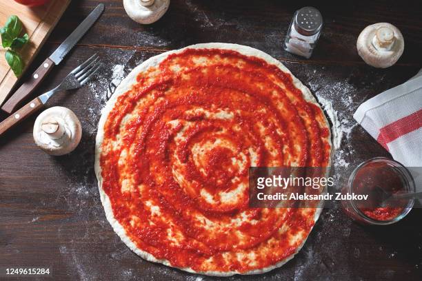 cooking italian vegetarian pizza with vegetables and mushrooms at home, on a wooden table. ketchup is smeared on the dough. step-by-step instructions, do it yourself. step 3. - tomato paste stock pictures, royalty-free photos & images