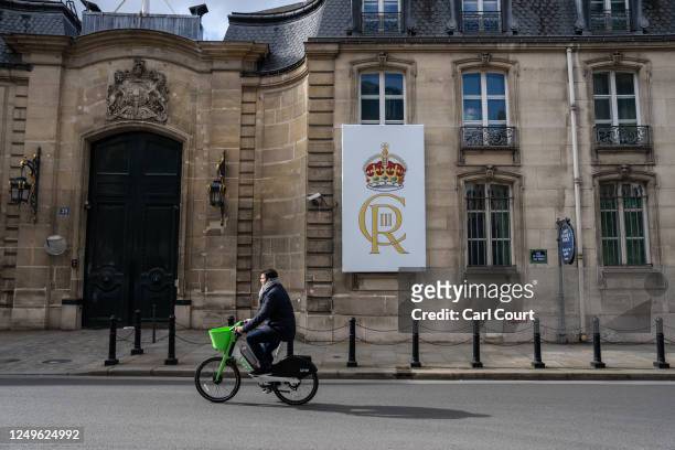 Man cycles past a banner bearing the crest of King Charles III displayed outside the residence of the British ambassador on March 27, 2023 in Paris,...