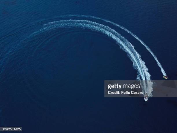 summer water sport fun rides. aerial view of a speedboat pulling an inflatable fun ride at the beach. - malta aerial stock pictures, royalty-free photos & images