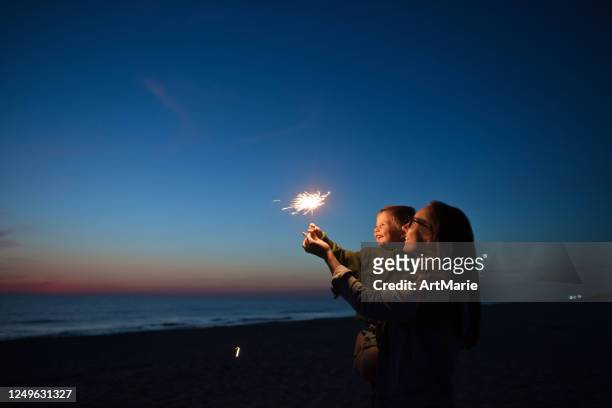 familie mit wunderkerzen am strand bei sonnenuntergang - sparkler firework stock-fotos und bilder