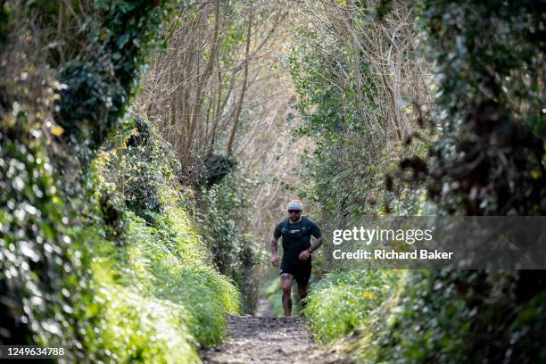 Man runs up a muddy rural track and into the distance in Mawnan Smith, on 19th March 2023, in Mawnan Smith, Cornwall, England.