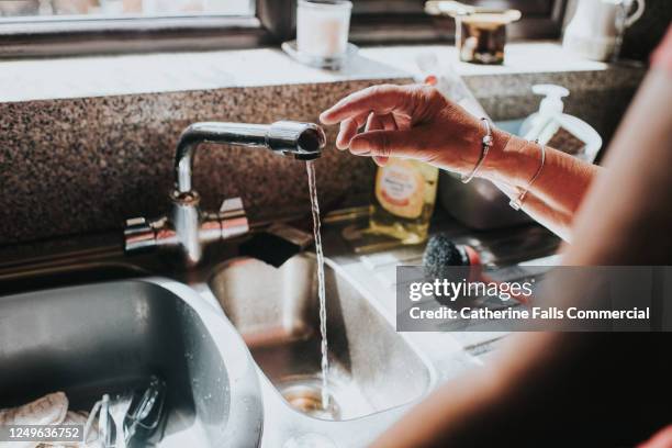 woman touches a chrome tap in a kitchen - washing tub stockfoto's en -beelden