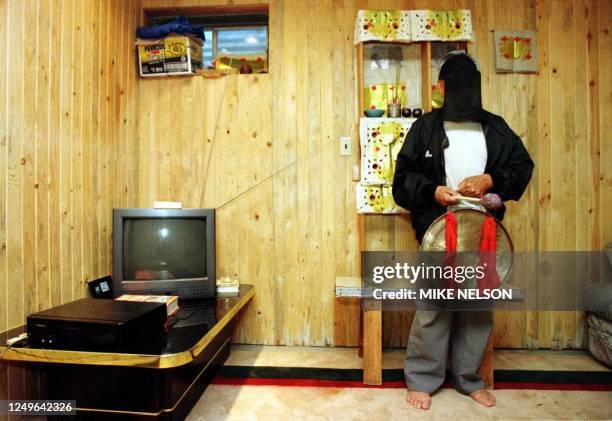 By Karen Lowe Kia Moua a Hmong shaman , with his face covered, stands holding a drum in front of an altar in his Missoula, Montana basement 19...